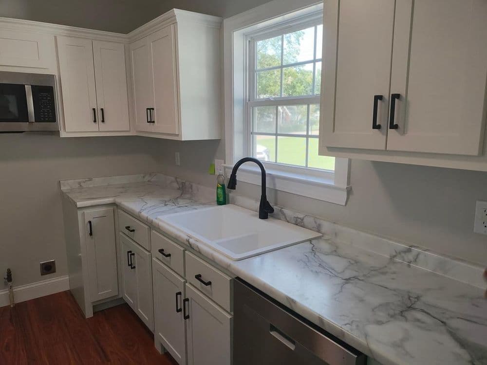 Modern kitchen with white cabinets, marble countertops, and a black faucet by the window.