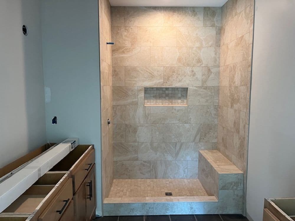 Modern walk-in shower with tiled walls, built-in niche, and bench seating in a bathroom remodel.