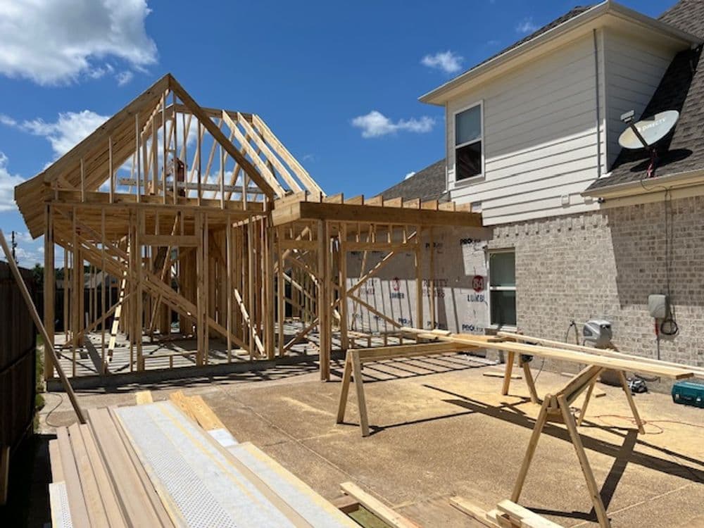 House under construction with wooden framing, tools, and blue sky in the background.
