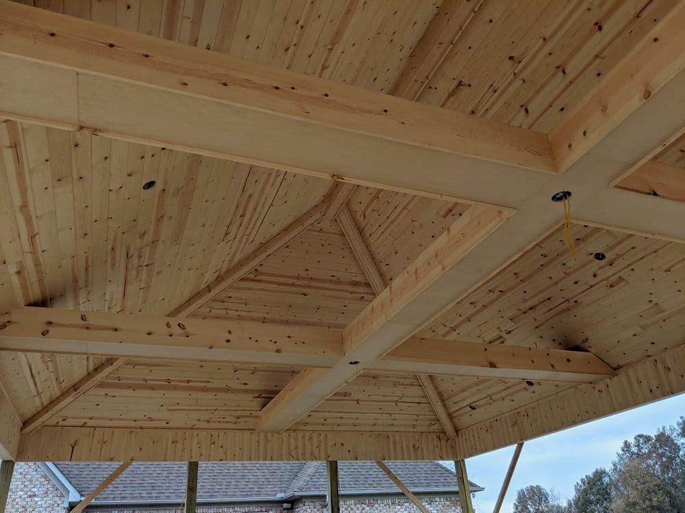 Interior view of a wooden pavilion ceiling with exposed beams and natural wood finishes.