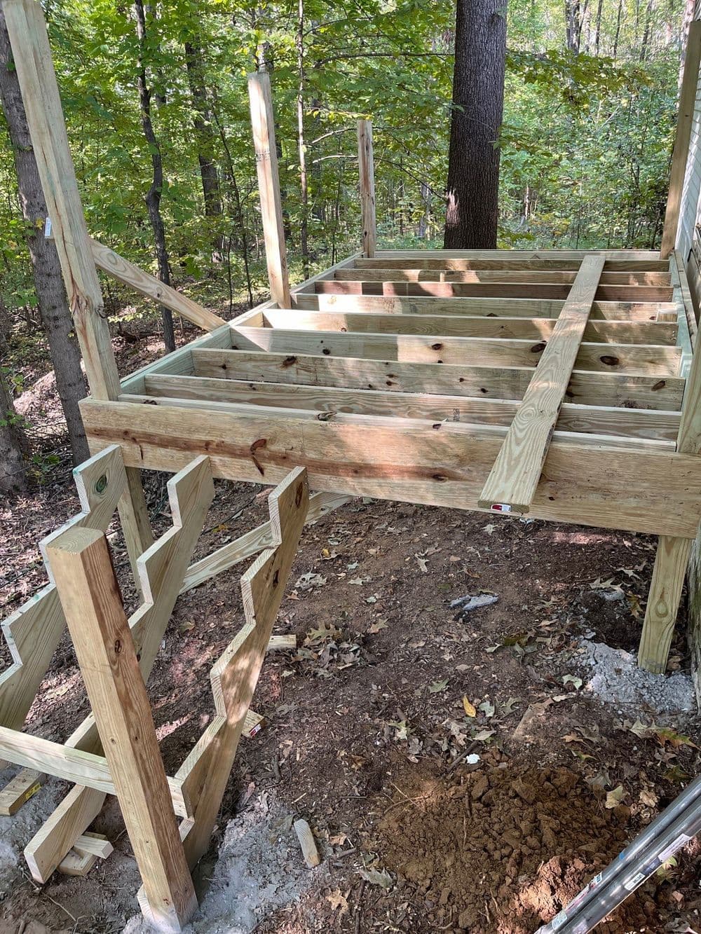 Wooden deck frame under construction in a forested area with stairs.