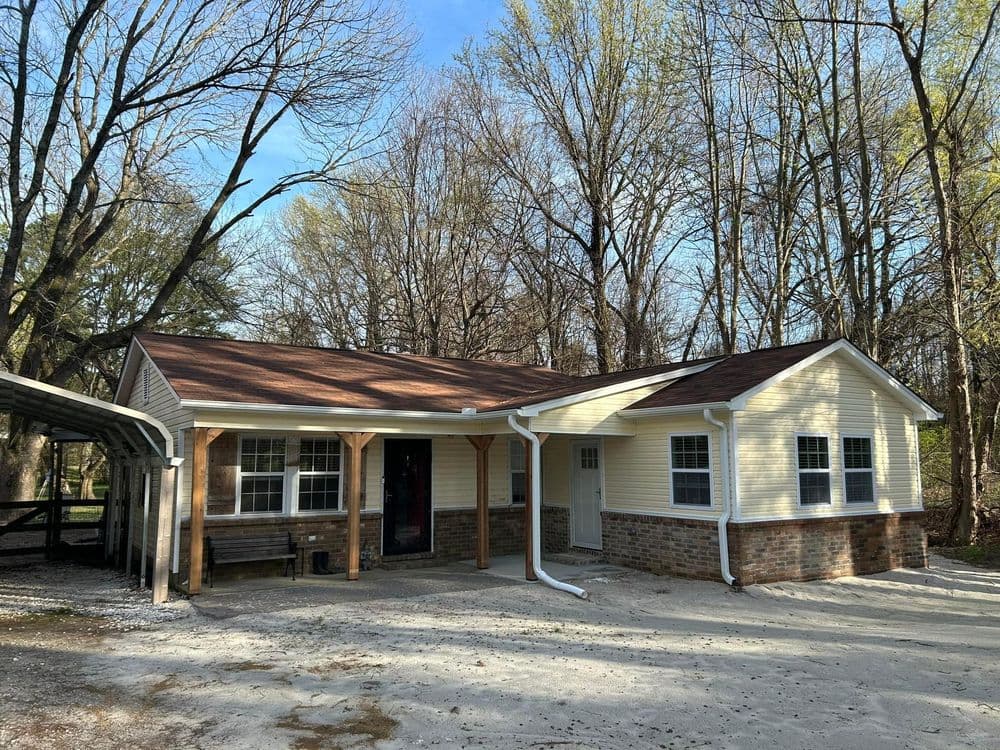 One-story home with brick accents, surrounded by trees, featuring a welcoming porch.