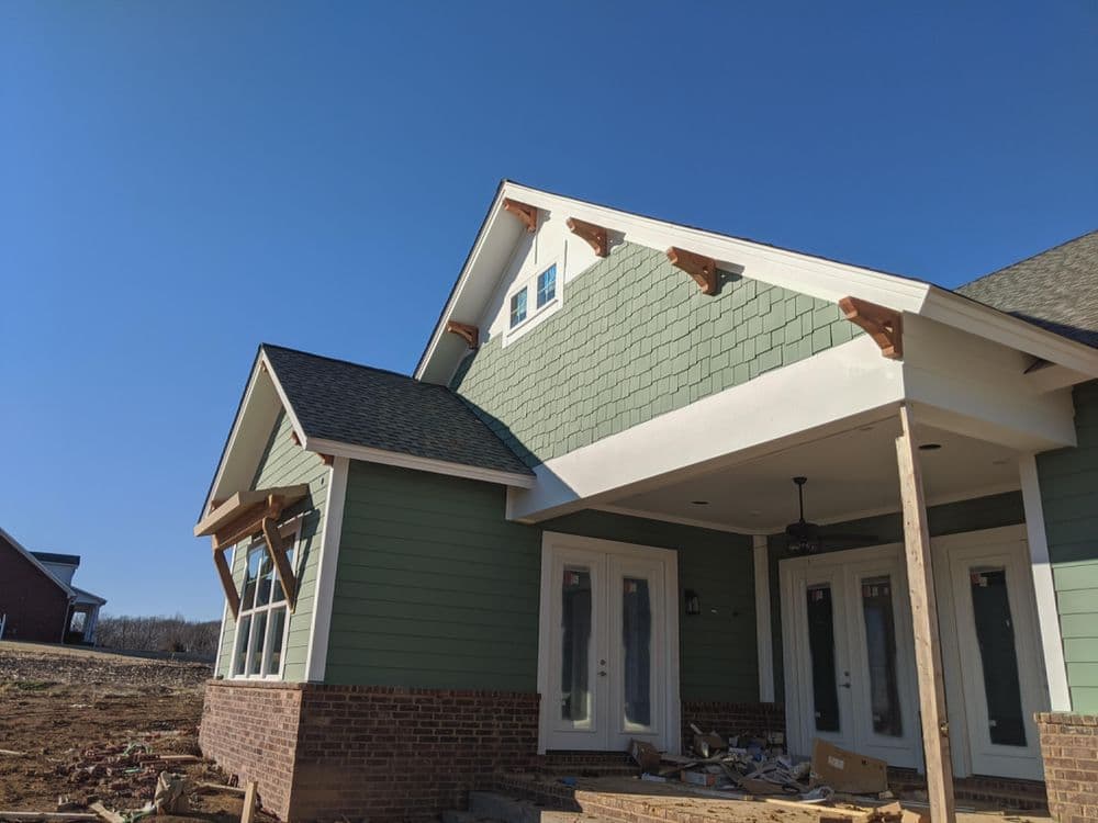 Newly constructed green house featuring a sloped roof and large windows under clear blue sky.