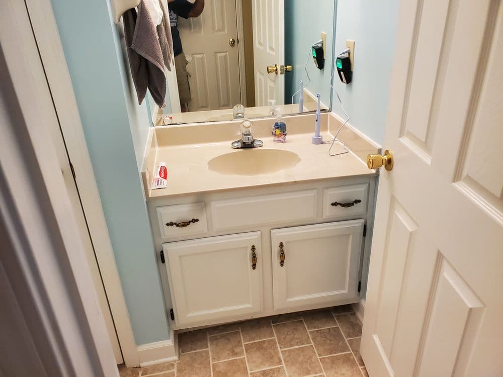 Small bathroom with white cabinetry, sink, and light blue walls, featuring a mirror and faucet.