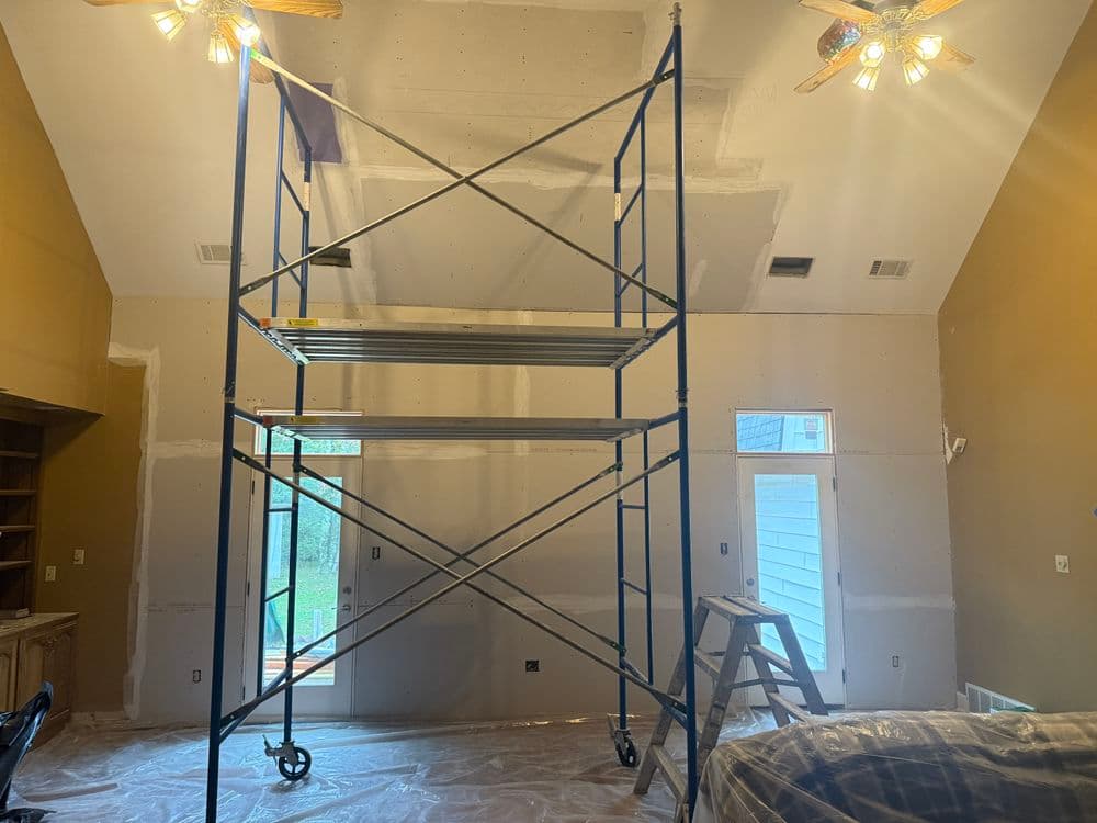 Scaffolding in a room with drywall installation and two ceiling fans.