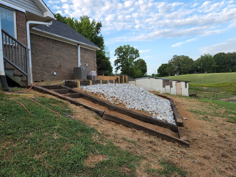 Gravel landscaping installation on sloped terrain beside a house with wooden edging.