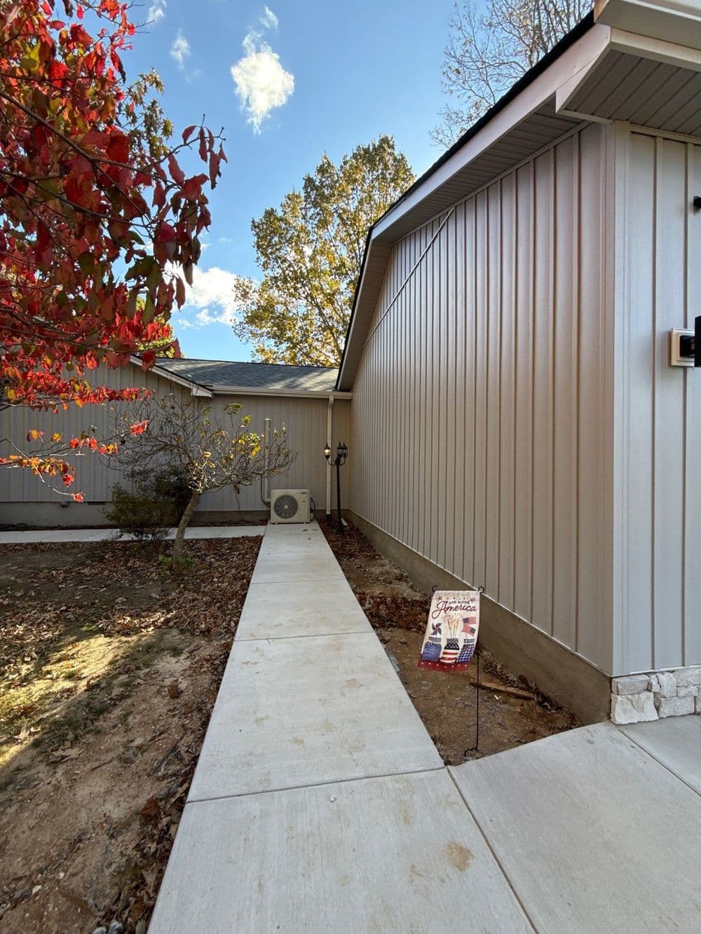 Sidewalk leading to a modern home with metal siding, autumn foliage, and a for-sale sign.