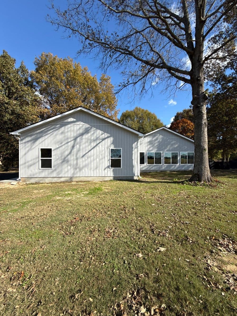 Modern metal building with large windows surrounded by trees and grass in a sunny landscape.
