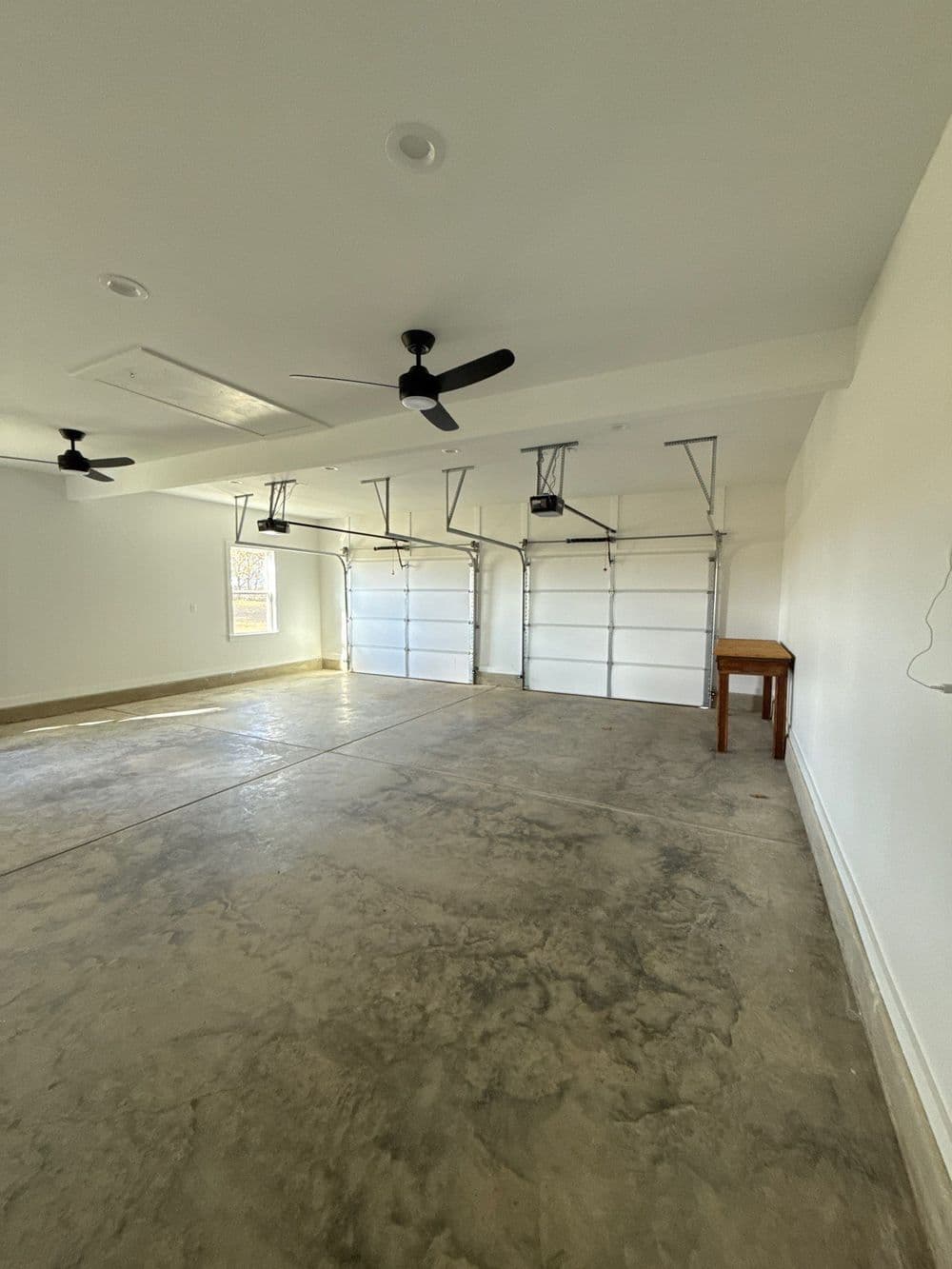 Spacious, empty garage with concrete floor, two ceiling fans, and double garage doors.