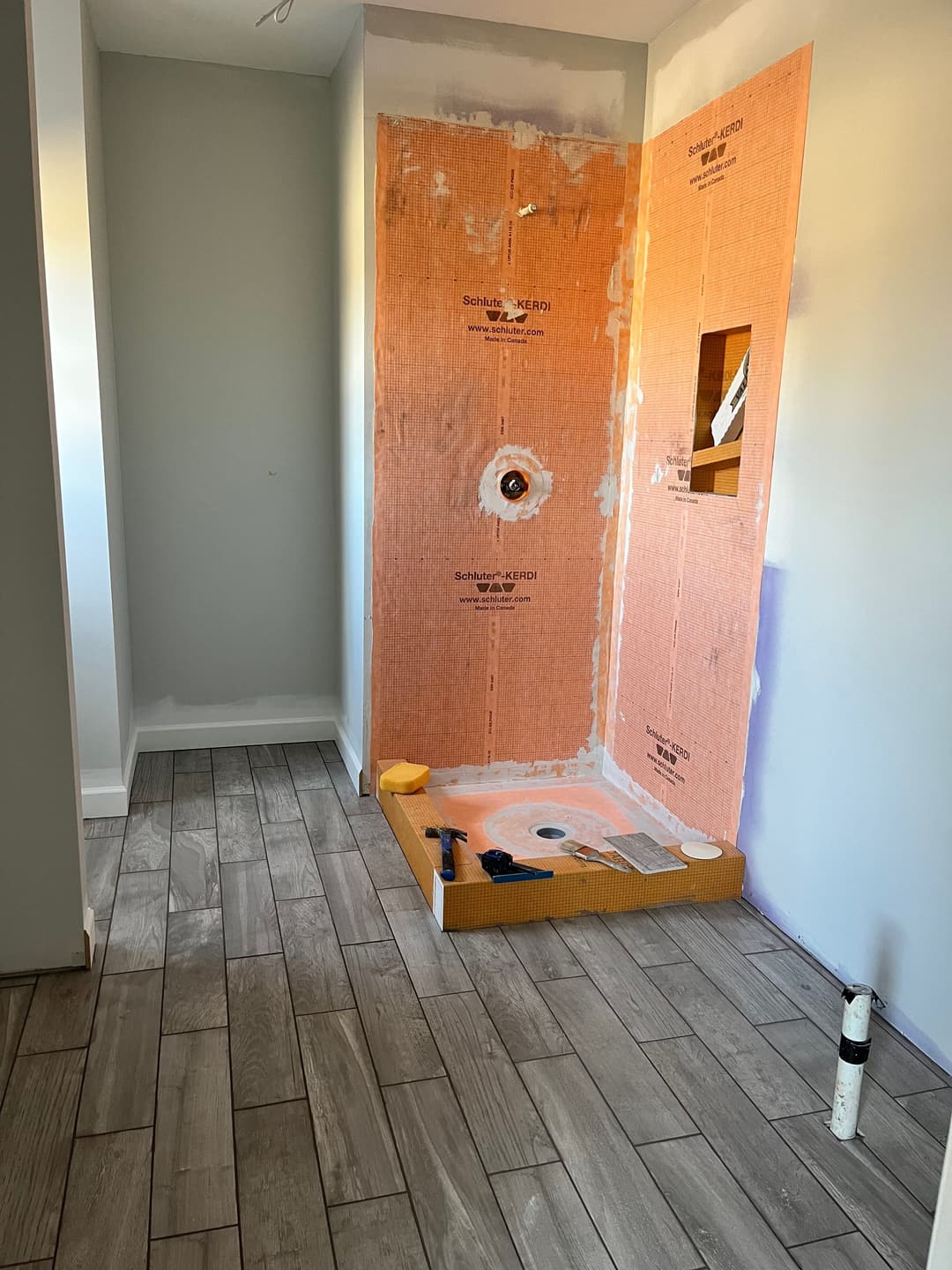 Home renovation showing a shower area under construction with orange waterproofing and tiled floor.