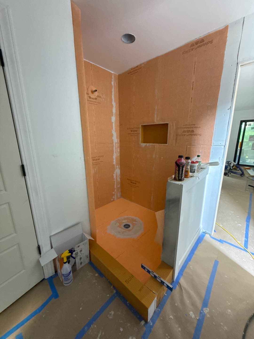 Under-construction shower stall with orange waterproofing membrane and drain installation.